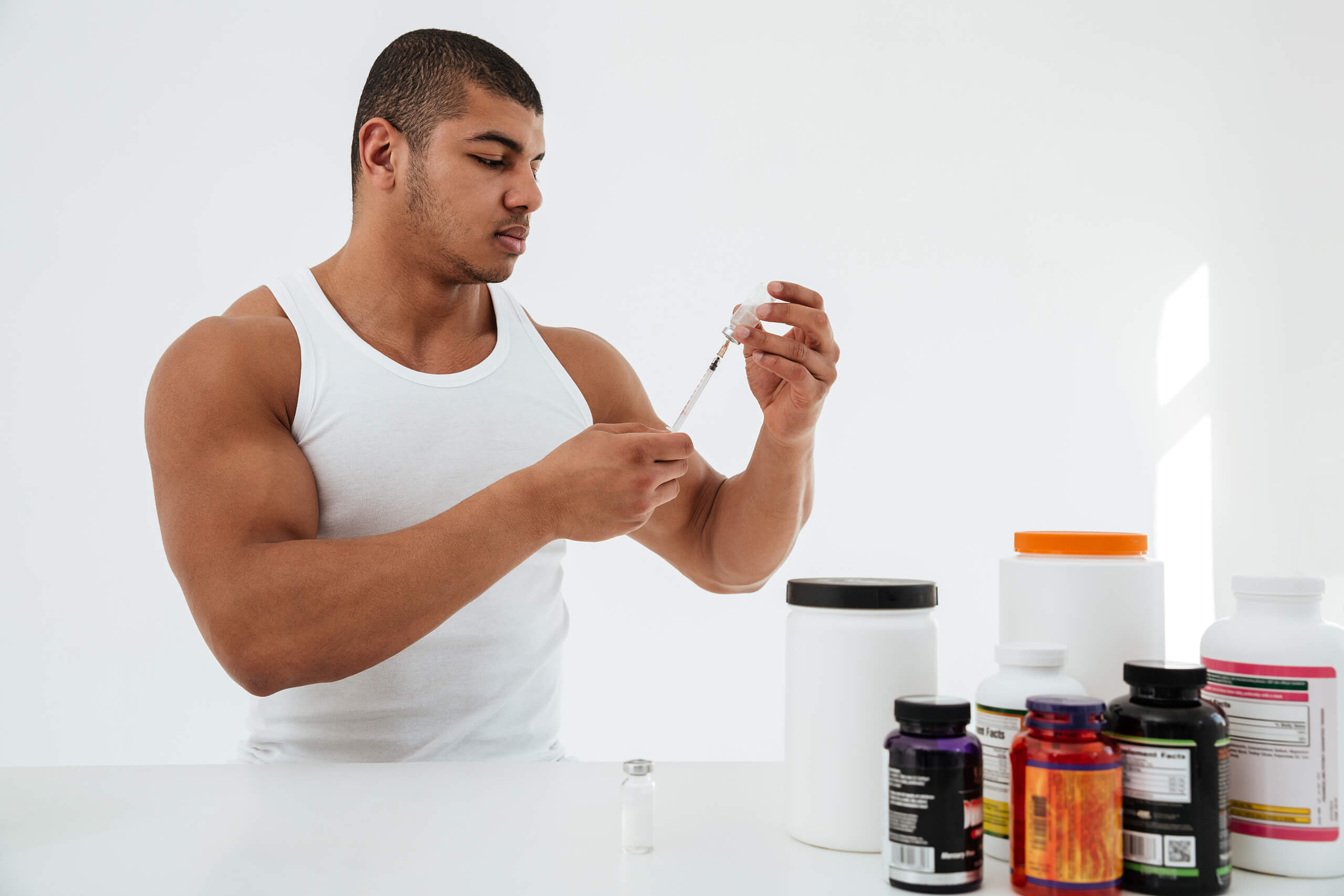 Muscular man preparing a lipotropic injection while comparing it to various oral supplement bottles on the table, illustrating the differences between injectable and oral fat-burning options